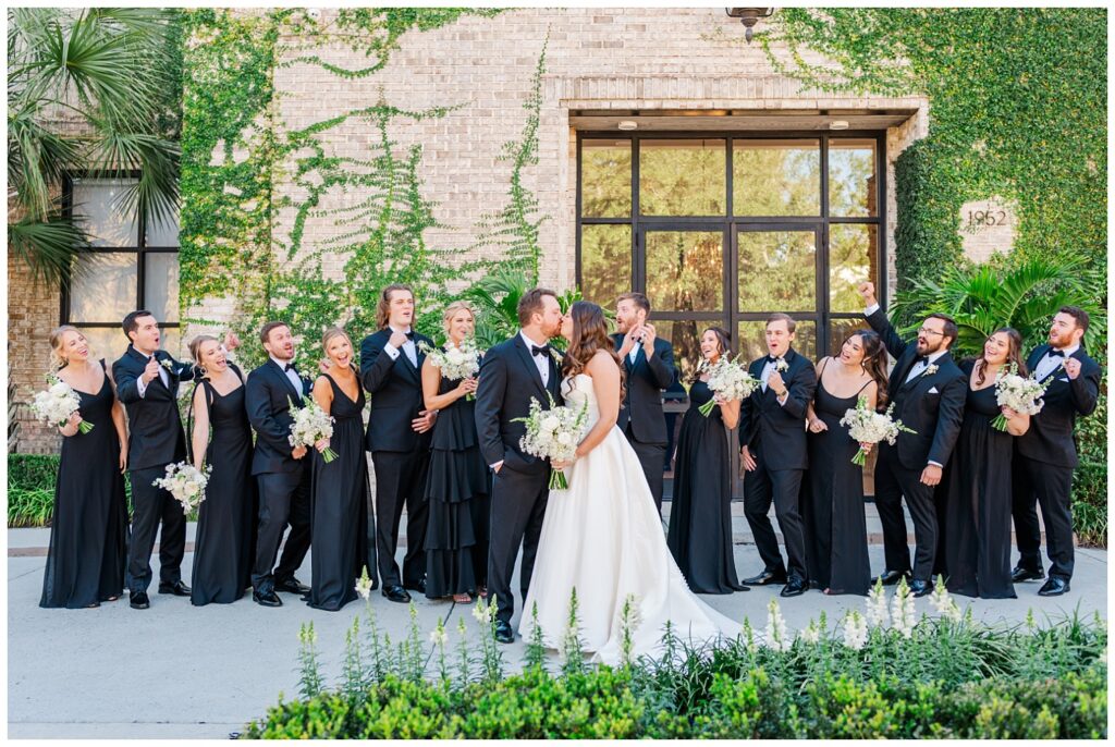 bride and groom kissing while the wedding party cheers them on from behind 