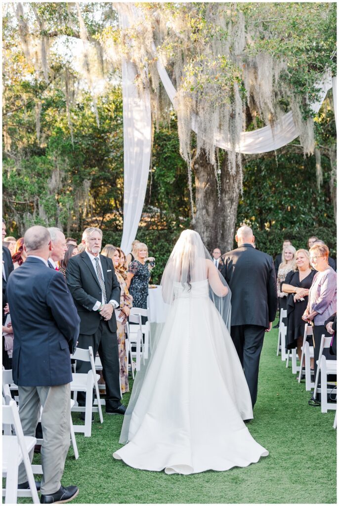 bride walking down the aisle outside with her dad towards a live oak tree in Wilmington 