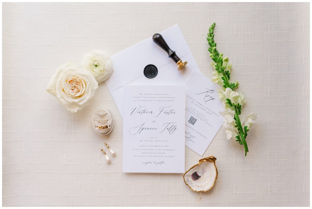 wedding flat lay with white roses, invitation suite, wax stamp, and oyster shell