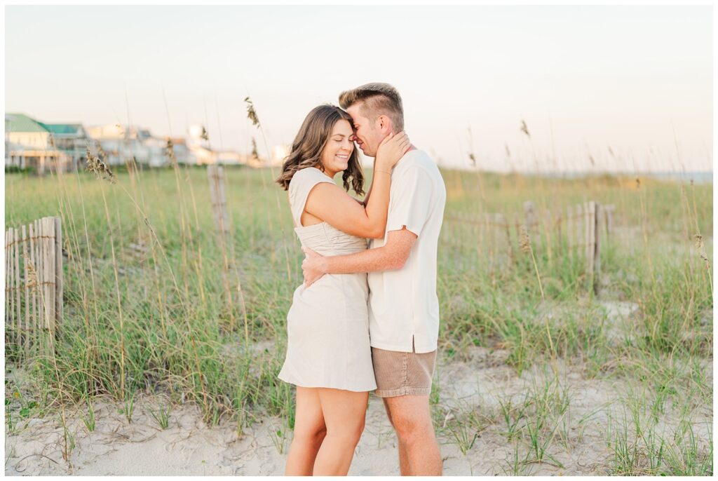engagement couple touching foreheads on the beach next to the dunes on Wrightsville Beach
