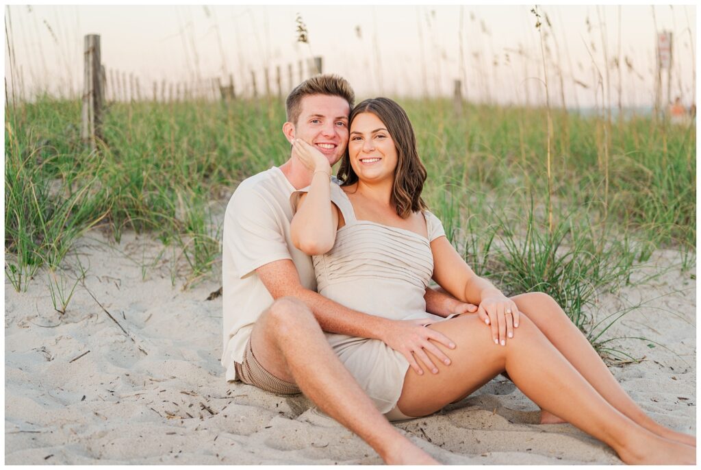 engaged couple sitting on the sand at Wrightsville Beach in Wilmington